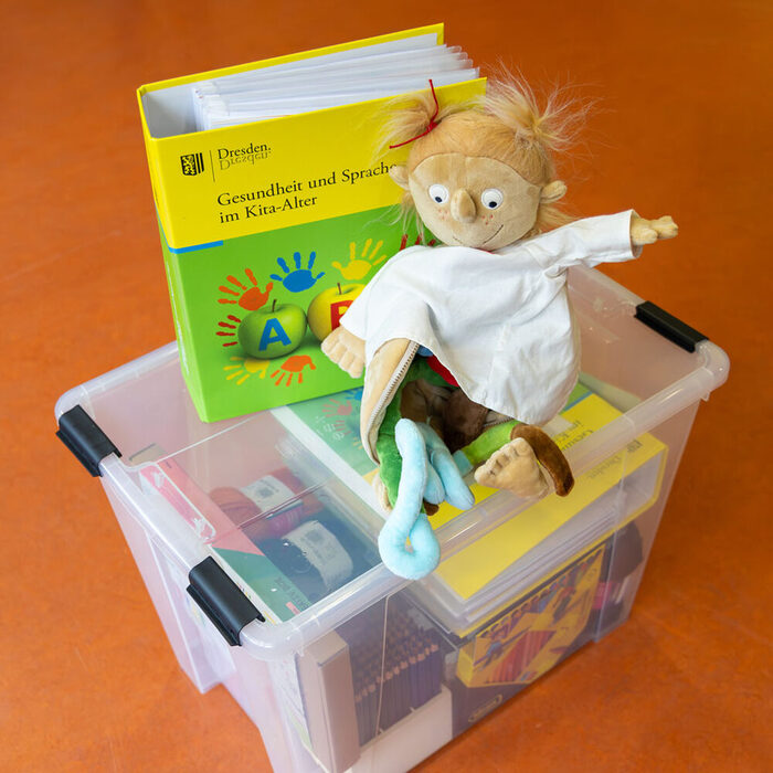 KitaGesund-Ordner und Materialkiste mit einer Puppe