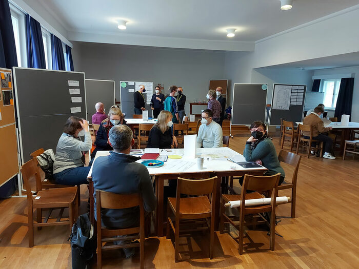 Menschen diskutieren beim Workshop an Tischen und einer Pinnwand im Gemeindesaal der Hoffnungskirche