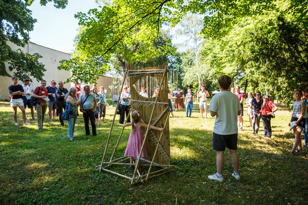 Ein Mädchen umfasst das Kunstprojekt aus Bambusstangen. Rundherum stehende Menschen schauen zu.