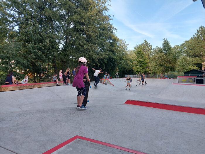 Skateanlage mit verschiedenen Elementen, im Vordergrund ein Mädchen mit Skatebord