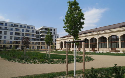Parkanlage mit Bäumen, Blumenbeeten, Weg und ehemaliger Orangerie im rechten Hintergrund