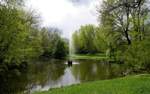 mit Bäumen umstandener Teich mit Fontäne im Park