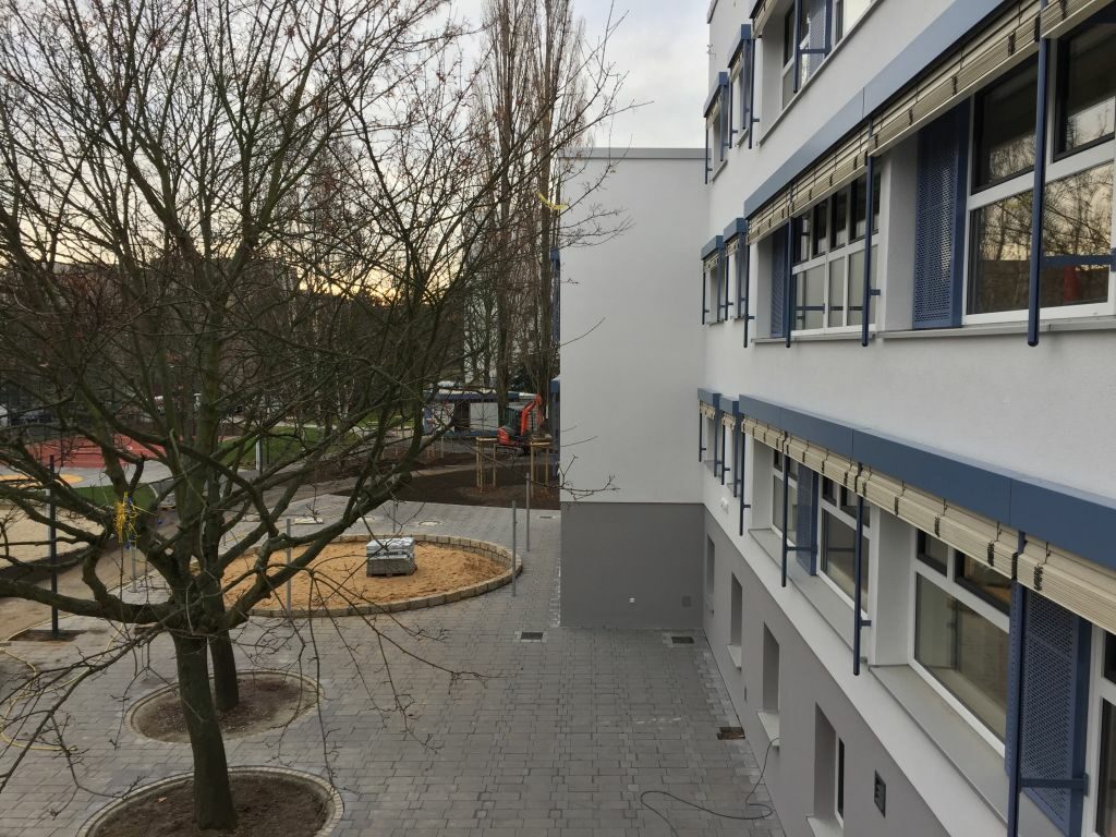 Seitlicher Blick in den Innenhof mit Bäumen und einem kreisrunden Sandkasten