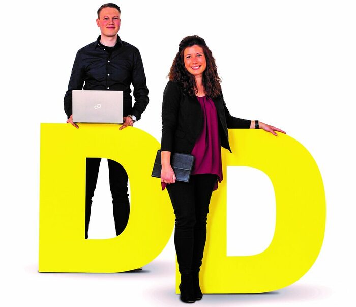 Zwei Personen stehen an großen gelben Buchstaben "D"