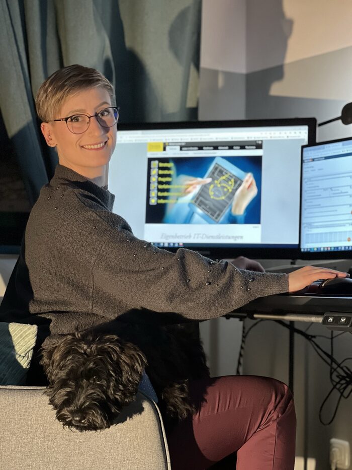 Frau sitzt vor einem Computer mit einem Hund auf dem Schoß
