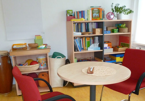 Beratungszimmer mit einem runden Tisch und Spielsachen im Hintergrund