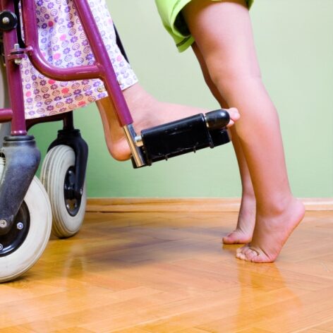 Kind auf Zehenspitzen vor einem Rollstuhl