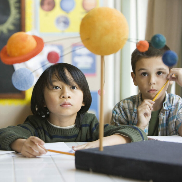 zwei Kinder sitzen vor einem Modell des Sonnensystems