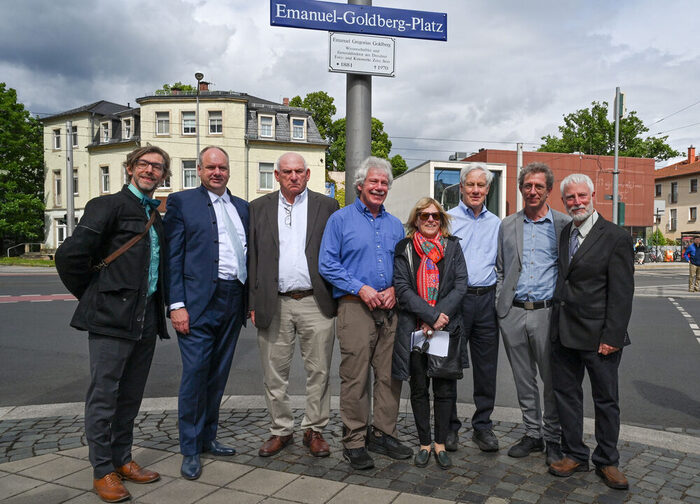 Acht Menschen stehen an einer Kreuzung vor einem Straßenschild