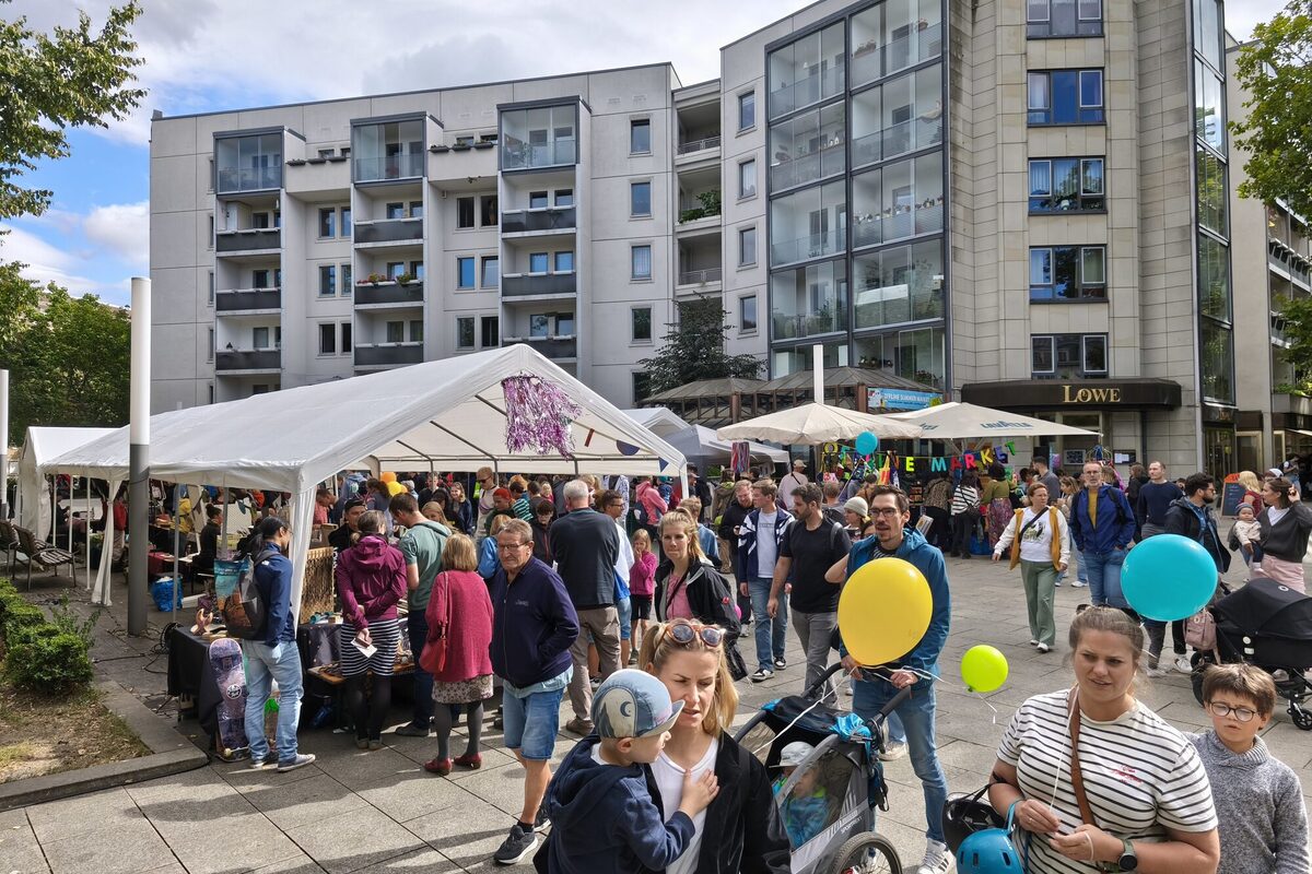 Pavillons mit Menschen auf einer Straße, dahinter Hochhäuser