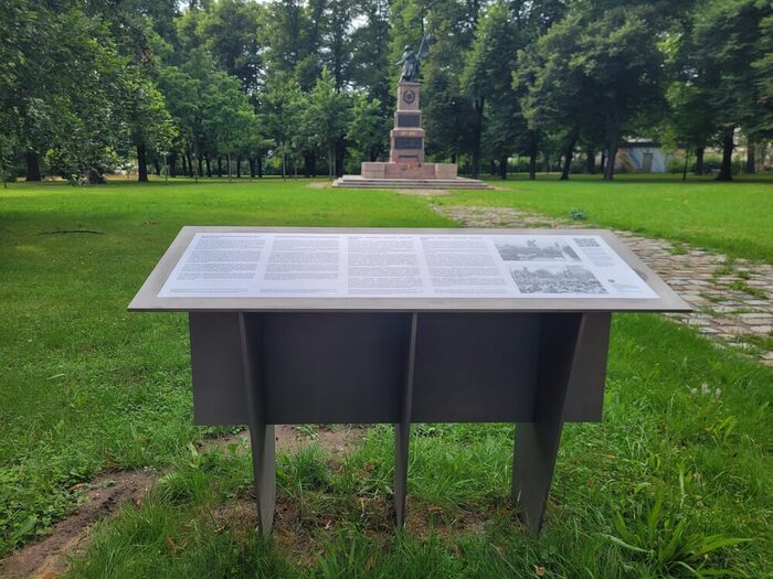 Tafel mit Texten und Fotografien, im Hintergrund das Denkmal der Roten Armee
