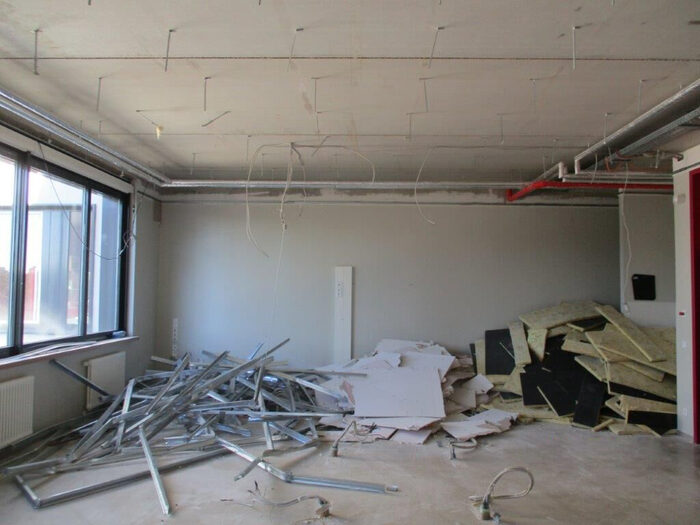 Das Bild zeigt ein entkerntes Klassenzimmer, bei welchem Boden und Decke entfernt wurden. Am Ende des Zimmers liegt Bauschutt.