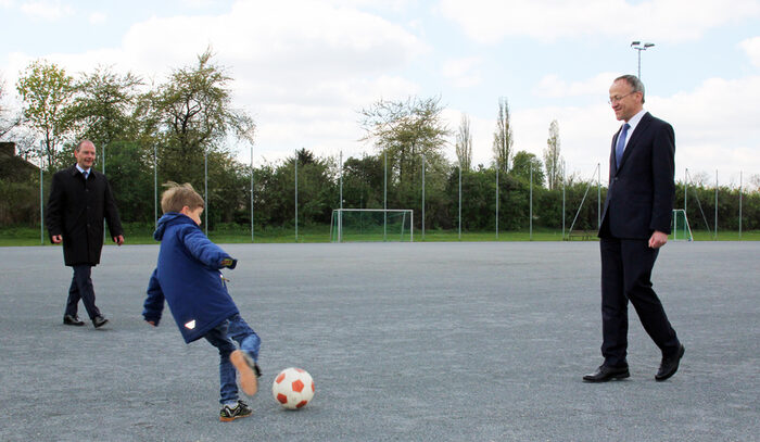 zwei Männer und ein kleiner Junge mit Ball auf einem Fußballplatz