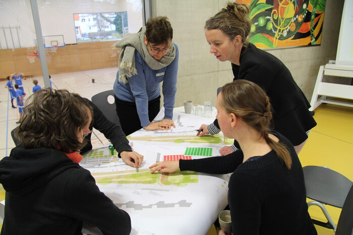 Vier Frauen stehen und sitzen um einen Lageplan