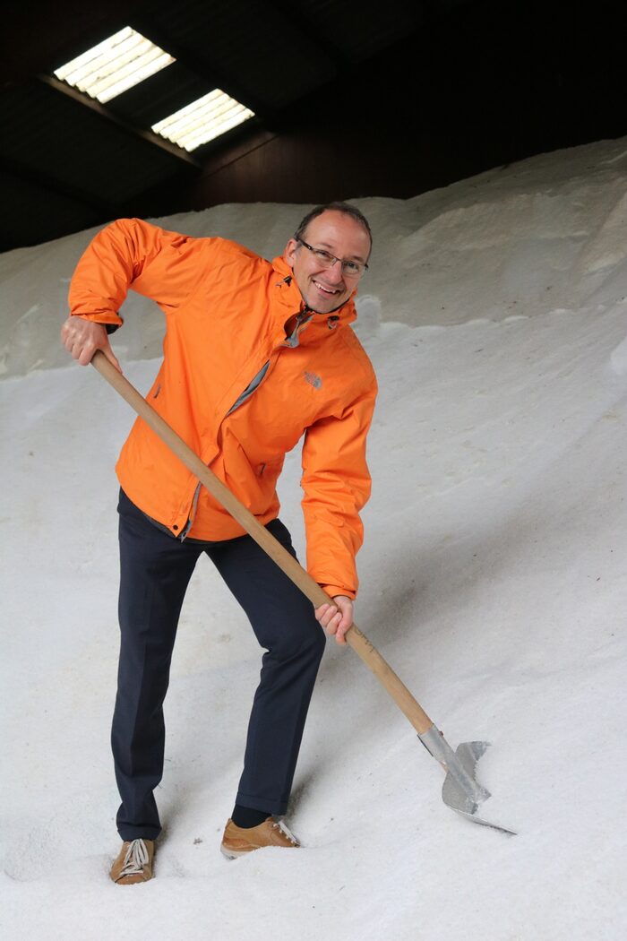 Dr. Franke in oranger Jacke mit Schaufel in einem Berg aus Streusalz