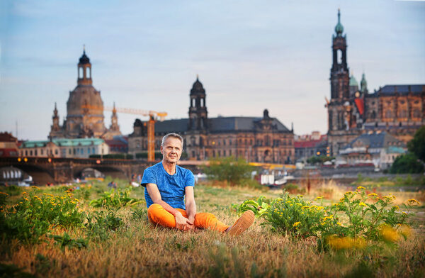 Michael Schindhelm auf eienr Wiese sitzend, im Hintergrund die Altstadtsilhouette Dresdens