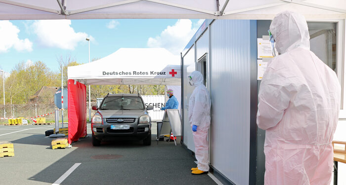 Auto in mobiler Teststation, rechts Menschen in Schutzkleidung