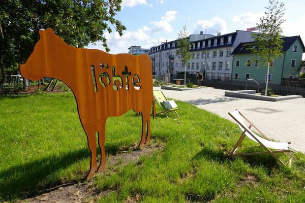 Metall-Kuh auf Grünfläche, im Hintergrund Häuser