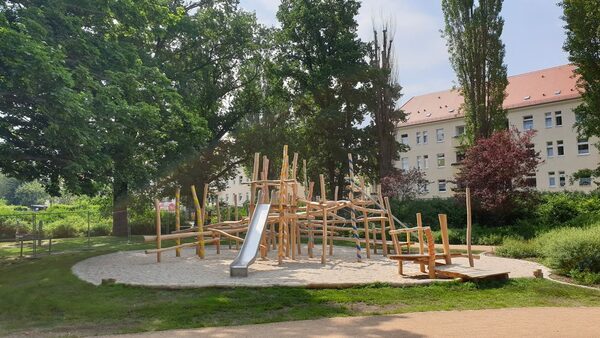 runde sandbedeckte Spielplatzfläche mit Holzklettergerüsten
