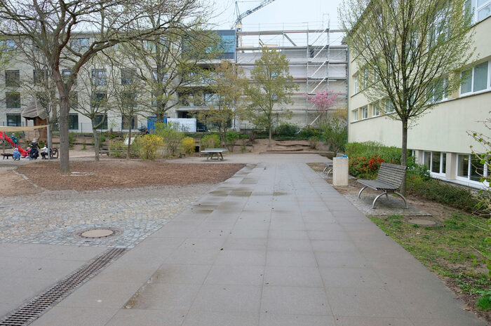 Foto vom Schulhof der 4. Grundschule, im Vordergrund Wege und Flächen mit Bepflanzung, im Hintergrund das Schulgebäude
