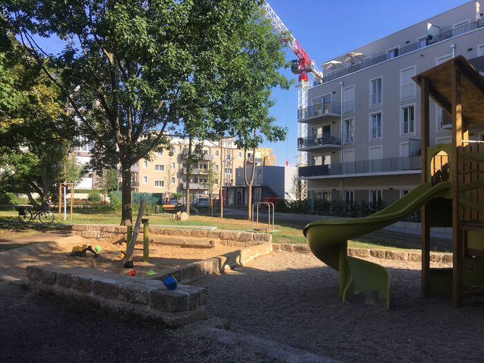 Blick auf die Grünanlage Grüne Mitte: Spieplatz mit Sandkasten und Klettergerüst umrahmt von Häusern