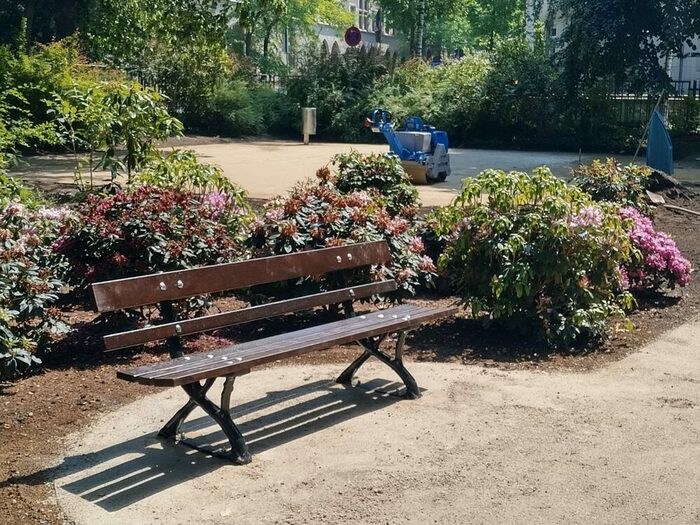 Bank vor grünen Büschen mit vereinzelten rosa Blüten
