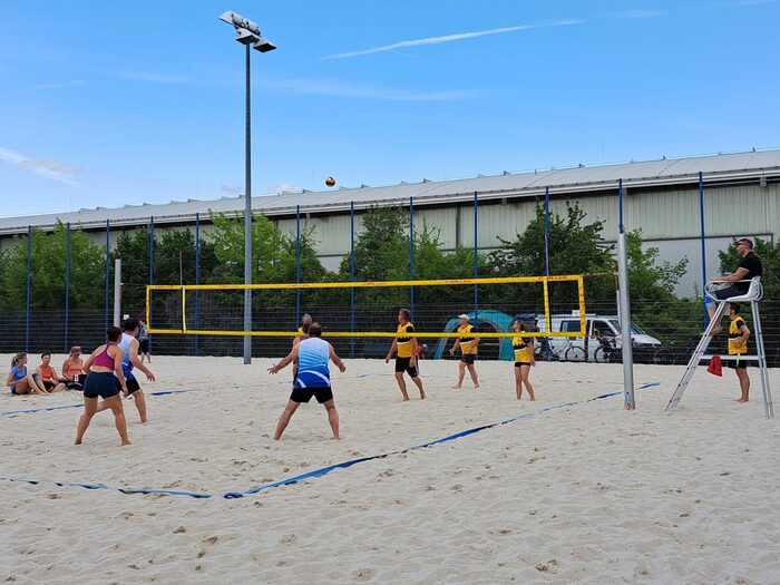 Menschen an einem Volleyballnetz im Sand, ein Ball fliegt