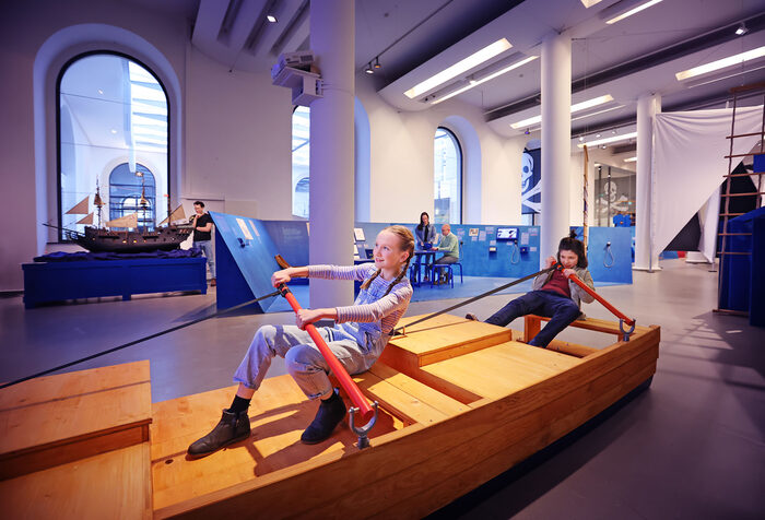 Kinder sitzen auf einem Modellboot und rudern