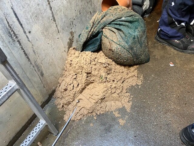 Sand neben einem grünen Sack auf nassem Boden im Innenraum