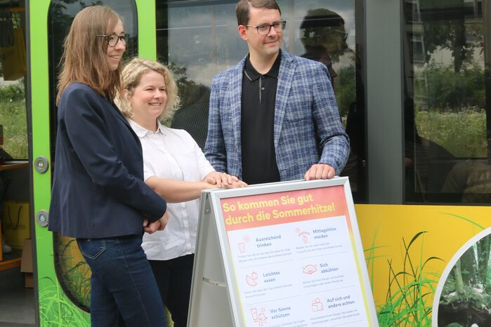 Drei Menschen stehen vor einem Aufsteller mit Tipps zum Schutz vor Hitze