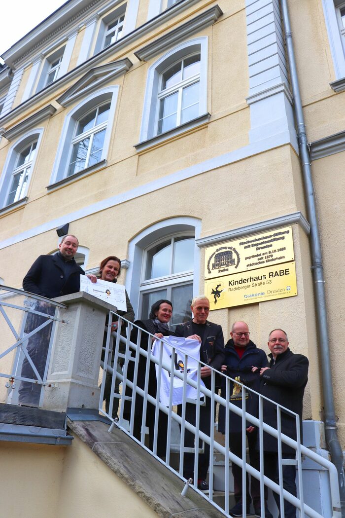 Menschen stehen vor dem Kinderhaus und halten einen Spendenscheck in der Hand