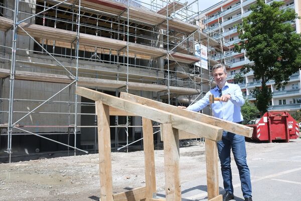 Mann mit Hammer vor einem Holzbock, in dem ein Nagel steckt