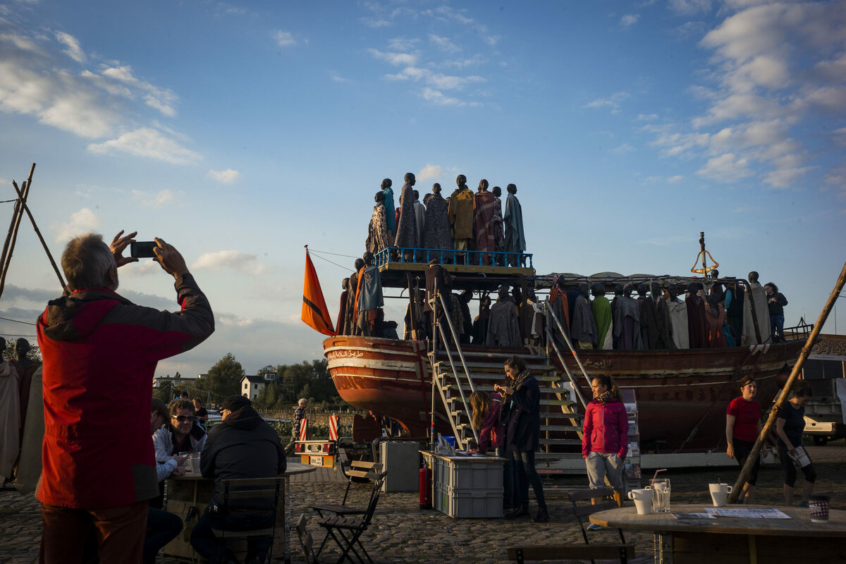 Mann fotografiert Boot mit Flüchtlingsskulpturen