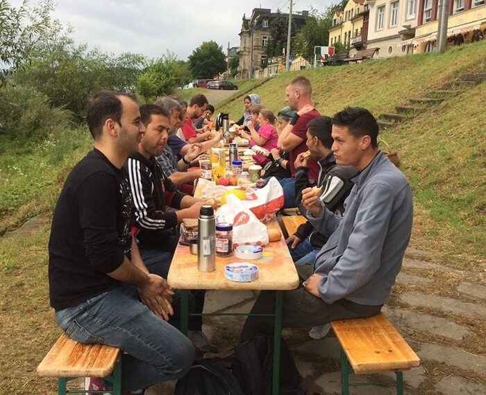 Flüchtlinge sitzen beim Frühstück an einer langen Tafel im Freien