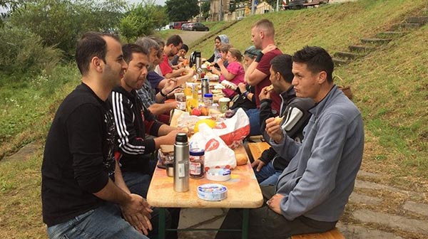 Flüchtlinge sitzen beim Frühstück an einer langen Tafel im Freien