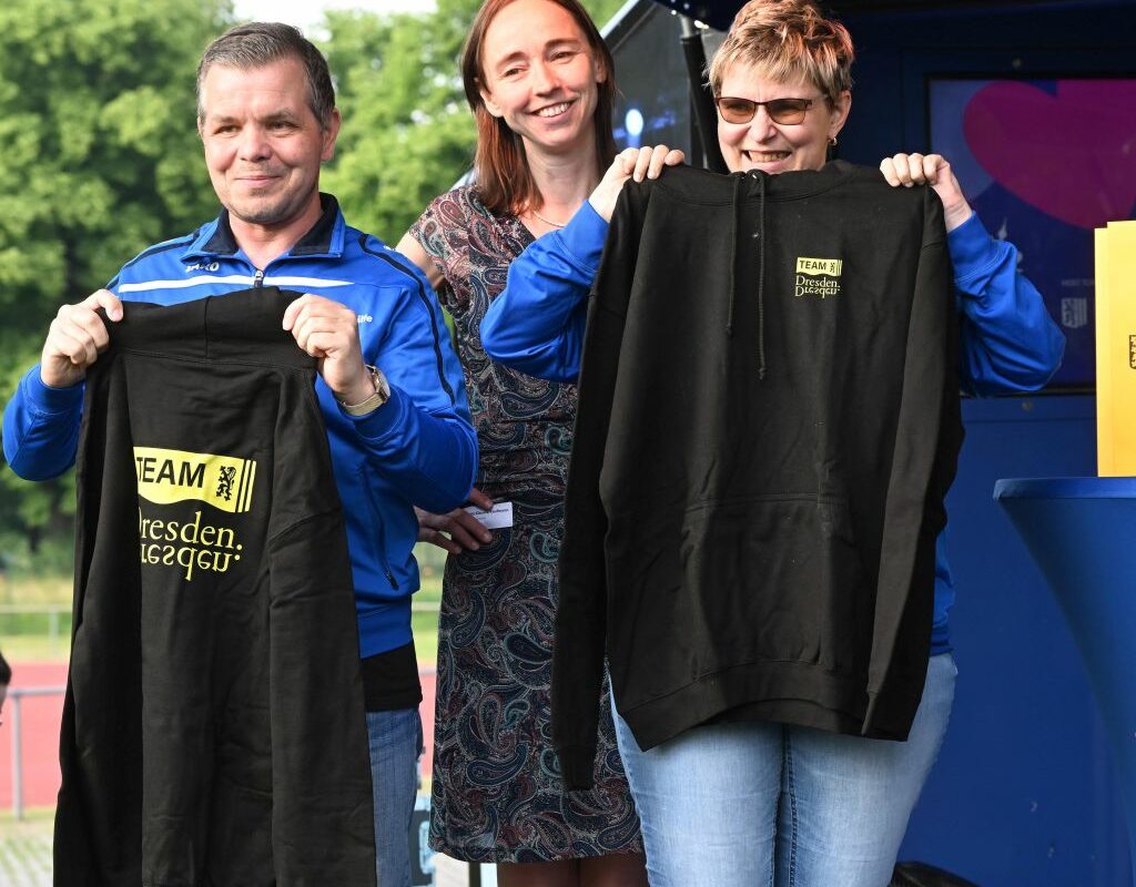 Sozialbürgermeisterin Dr. Kristin Kaufmann übergibt den Dresdner Special-Olympics-Teilnehmenden Frank und Dörte die Team-Dreasden-Hoodies