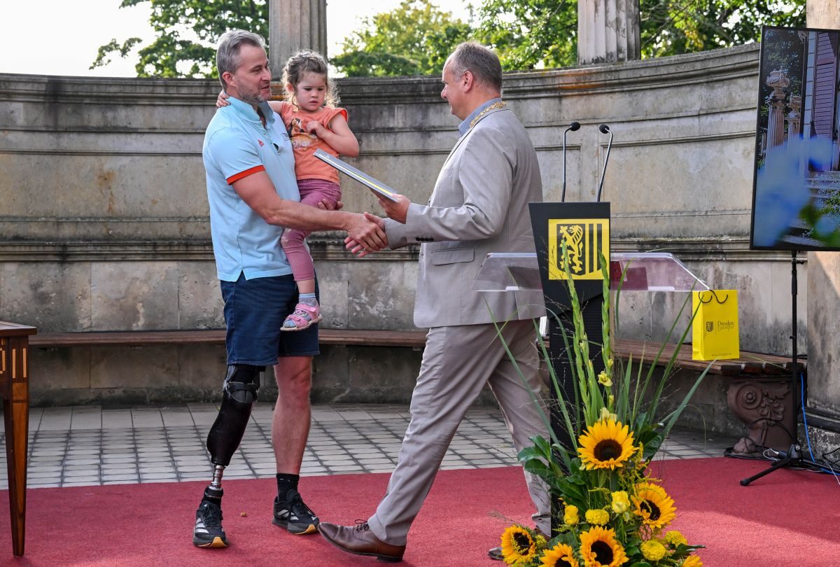 Oberbürgermeister Dirk Hilbert (rechts) gratuliert Preisträger Alexander Schiffler (links), auf dessen Arm seine Tochter