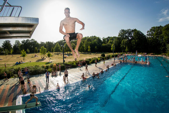 Ein junger Mann springt vom Sprungturm ins Wasserbecken eines Freibades
