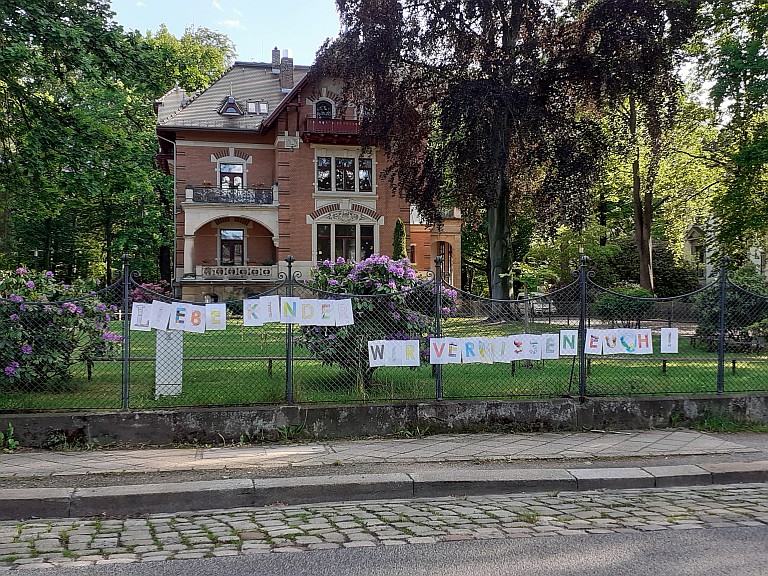 Von Erziehenden einer Kindertagesstätte am Zaum aufgehangene Zettel mit der Aufschrift "Liebe Kinder, wir vermissen euch"