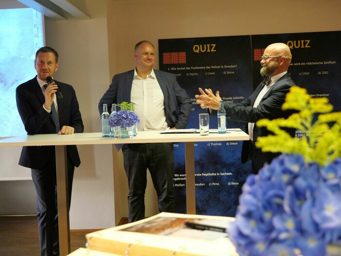 Ministerpräsident Michael Kretschmer, Oberbürgermeister Dirk Hilbert und Archivdirektor Prof. Thomas Kübler diskutieren an einem Stehtisch mit Getränken und Blumen