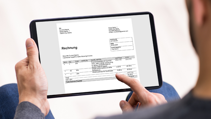 Ein Mann tippt mit seinem Finger auf ein Tablet. Auf dem Tablet ist eine Rechnung abgebildet.