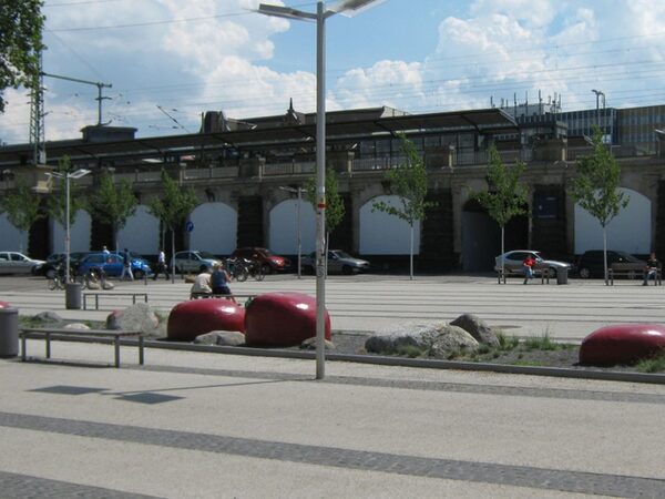 Das Bild zeigt den städtischen Teil des Vorplatzes an der DVB-Haltestelle mit dem künstlerisch gestalteten Weißeritzband und Sitzbänken