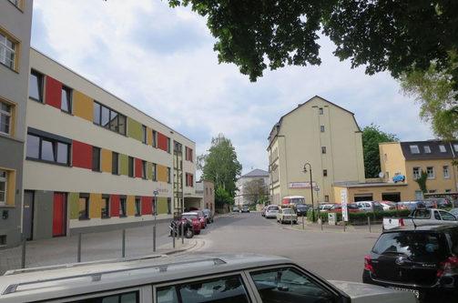 Das Foto zeigt den Anfang der Konkordienstraße von der Gehestraße aus fotografiert. Links ist die neue Kita "Concordia" zu erkennen, rechts ein Kfz-Betrieb. Die Straßenränder sind mit parkenden Pkw zugestellt.