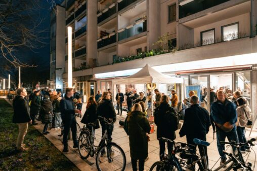 Volles Haus zur Vernissage der Fotoausstellungen im Ladengeschäft der Hauptstraße 42-44. Viele Besucherinnen und Besucher stehen auf der Straße vor dem Gebäudeeingang.