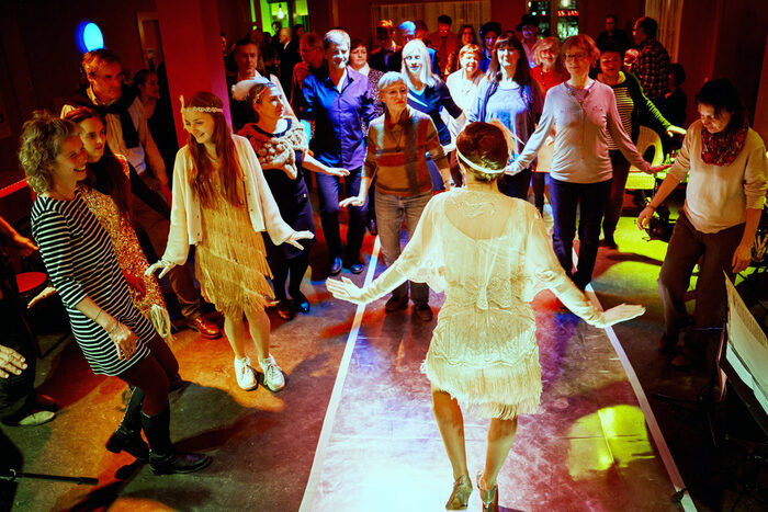 Tanzen wie in den 20ern gehörte ebenfalls zum Jubiliäumsprogramm "Alles Kästner". Zu sehen ist eine Tänzerin im Charleston-Kleid, die einer Gruppe tanzfreudiger Bürgerinnen und Bürger die Tanzschritte zeigt.