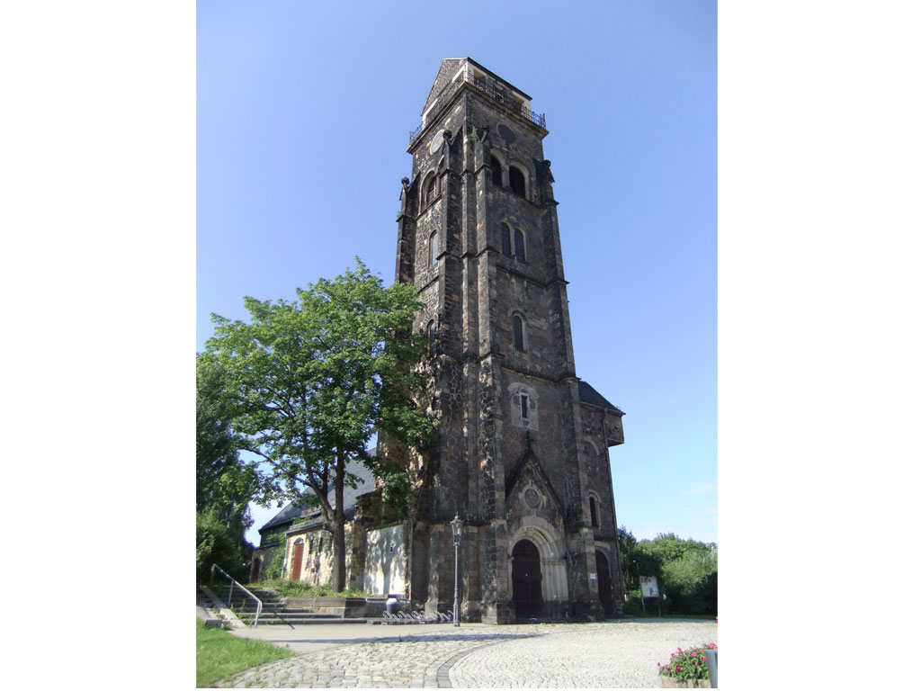 Auf dem Foto steht der Betrachter direkt vor dem Eingang und dem Turm der Fridenskirche. Der Vorplatz ist ordentlich und neu gepflastert.