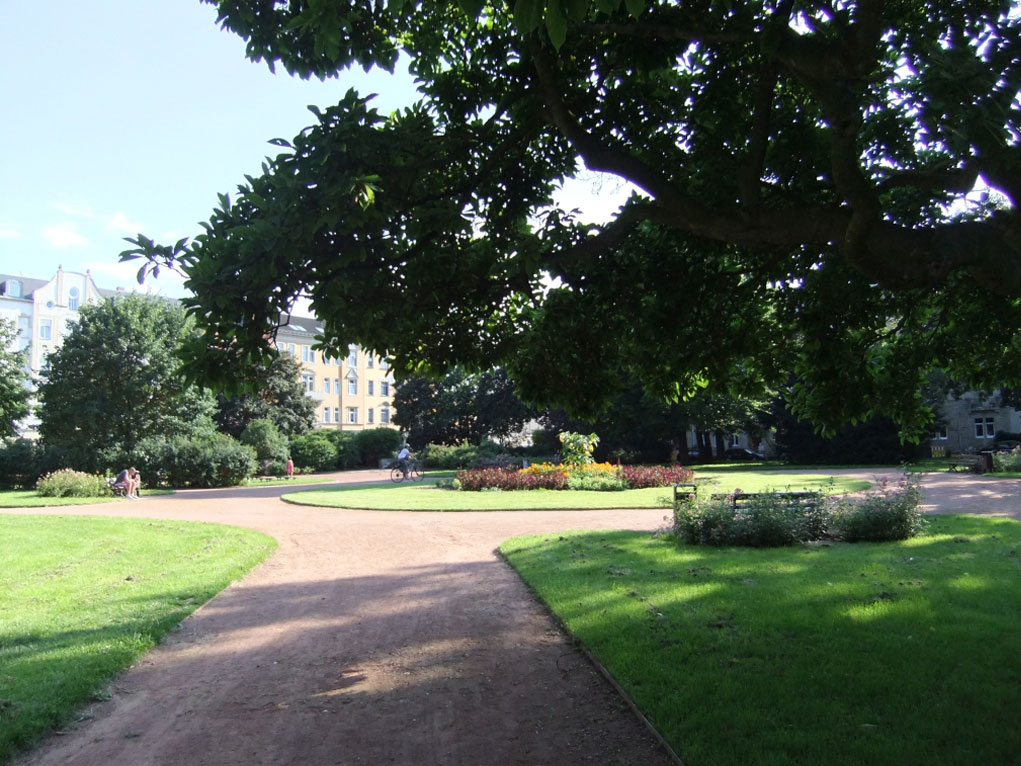Auf dem Foto ist der Blick in die Grünanlagen am Conertplatz eingefangen, wo der Weg um ein rundes Beet herumgeführt ist.