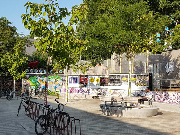 Blick auf die Sitzgestaltung des mit Bäumen und Fahrradständern komplettierten Scheuvorplatzes.