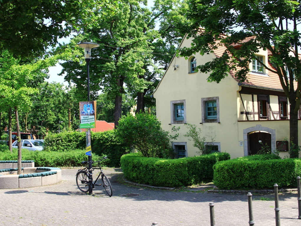 Das Foto zeigt einen gestalteten Platz mit Rundbänken und grünen Hecken, vor saniertem Fachwerkhaus.