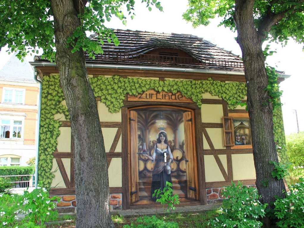 Das Foto zeigt eine kleine Station der DREWAG, welche mit einem Grafity verziert ist auf welchem eine Szene aus der Schenke "Zur Linde" dargestellt ist.